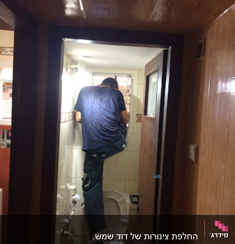 אדם עובד על צנרת מעל אסלה בחדר אמבטיה קטן